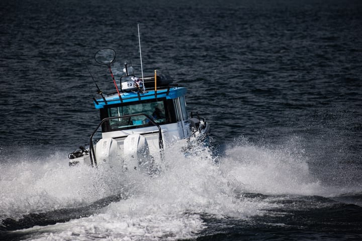 A white and blue cabin boat with triple outboards cuts through dark water, throwing spray on both sides.