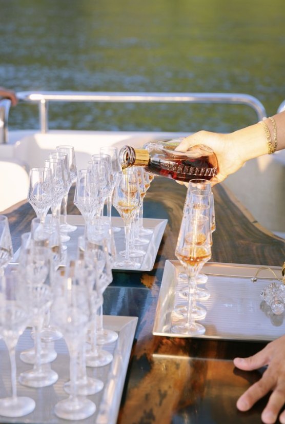 Cognac being poured into rows of glasses on a yacht table
