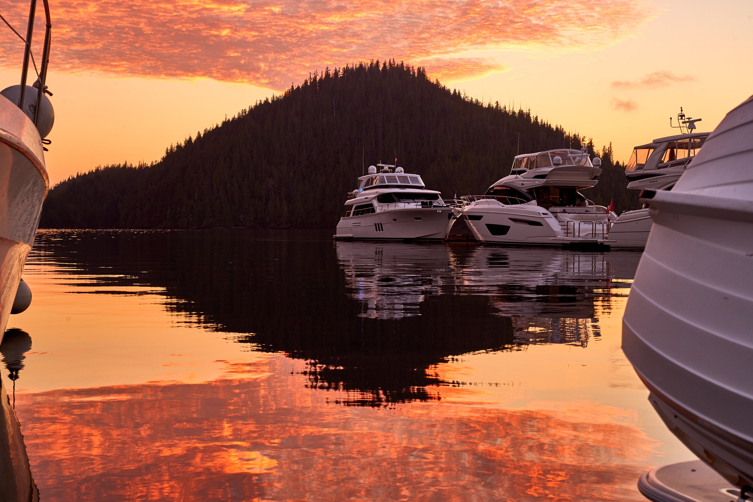 Motor yachts at a dock under an orange sunset sky reflected in still water
